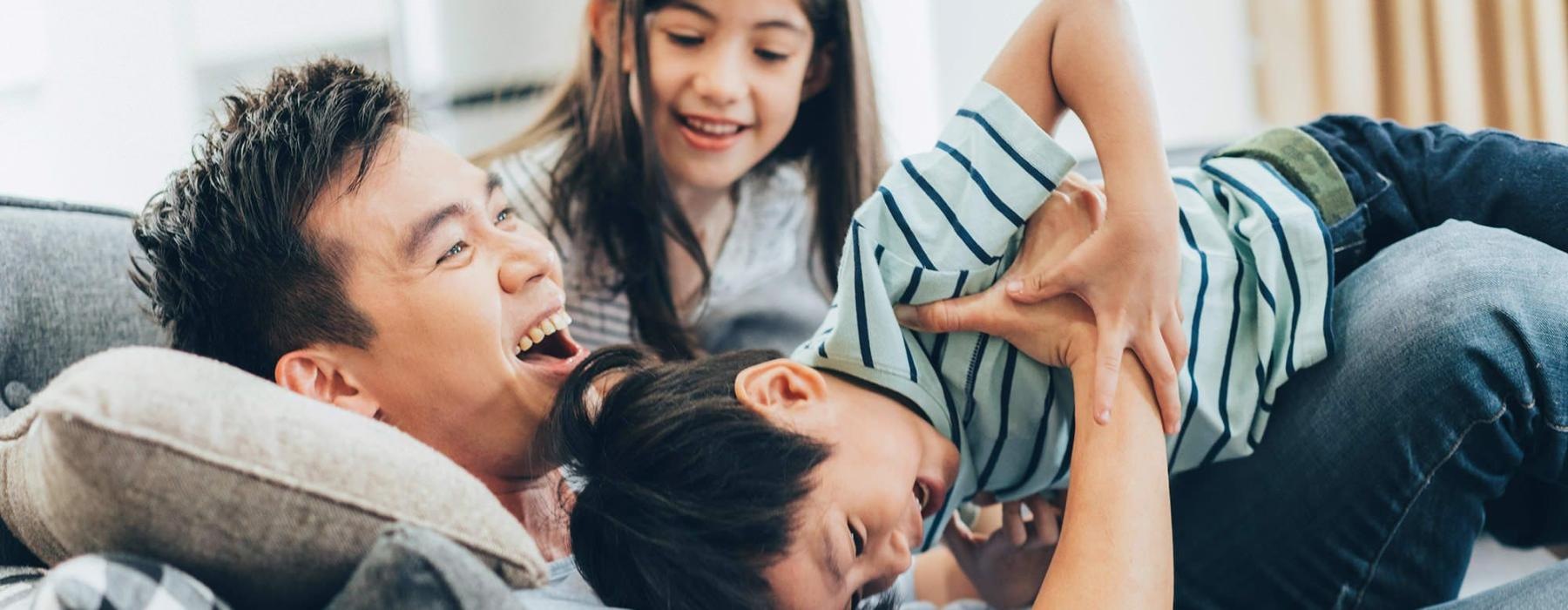 father plays on a couch with his young children